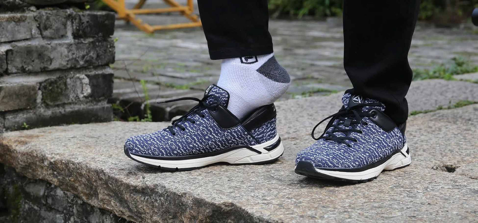 A pair of navy and white marled knit Zeba sneakers worn with white socks, stepping onto a stone step outdoors